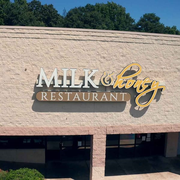 The Milk & Honey Restaurant sign on a light brick building under a clear blue sky.