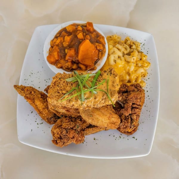 Milk & Honey's fried chicken and wings with mac and cheese and candied yams on a white plate.