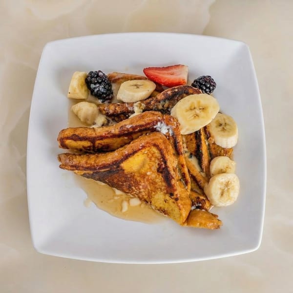Golden French toast triangles with sliced bananas, blackberries, and strawberries on a white plate.