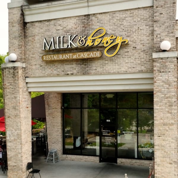 Exterior of Milk & Honey restaurant with brick facade, large windows, and outdoor patio seating.