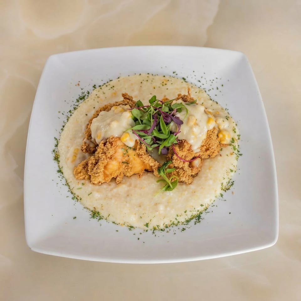 Milk & Honey's shrimp and grits, topped with creamy sauce and microgreens, on a white square plate.