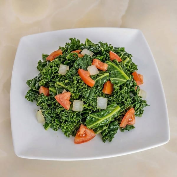 A vibrant green kale salad with diced tomatoes and onions on a white square plate.