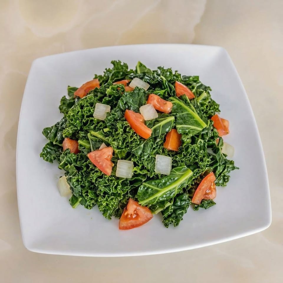 A vibrant green kale salad with diced tomatoes and onions on a white square plate.